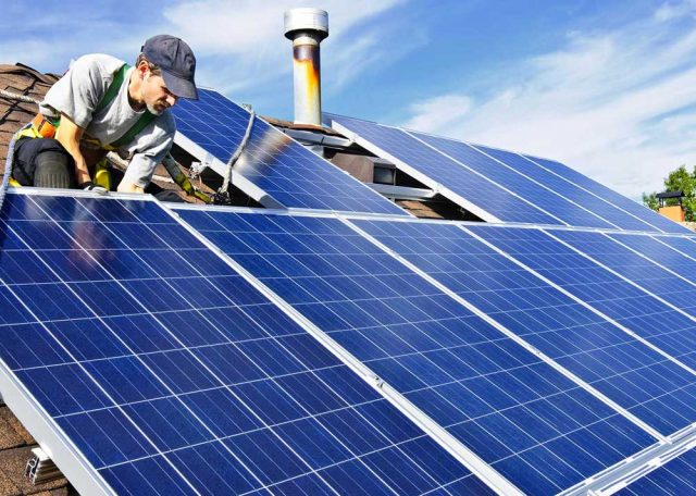 Worker installing solar panels on suburban roof